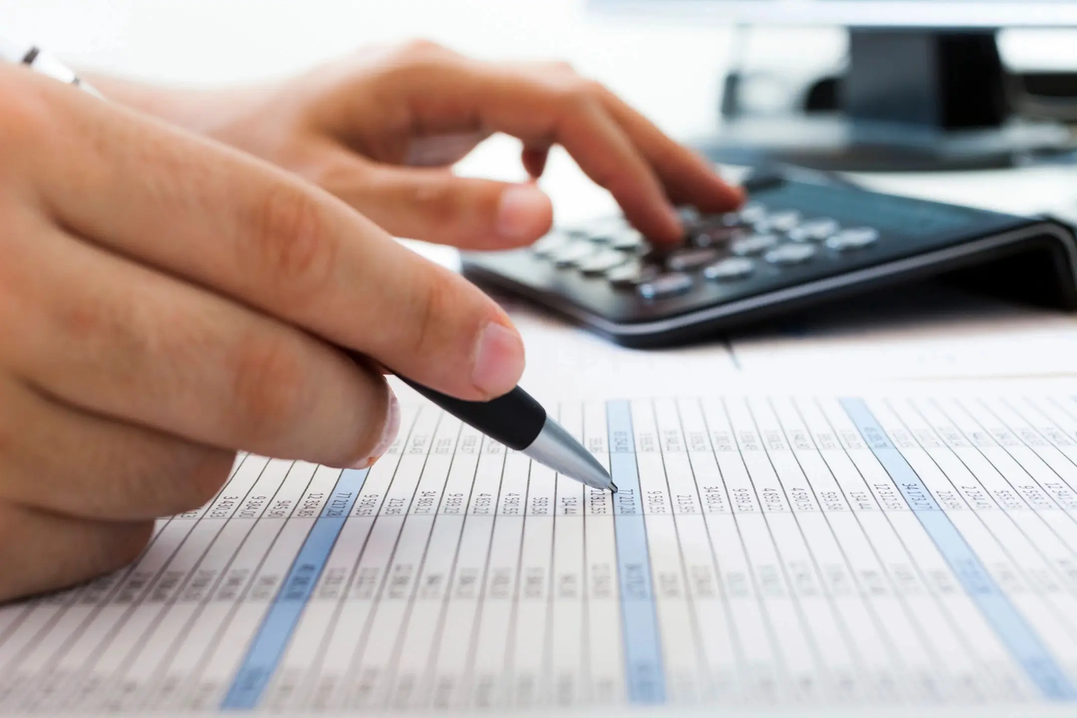 Person reviewing spreadsheet with pen and calculator